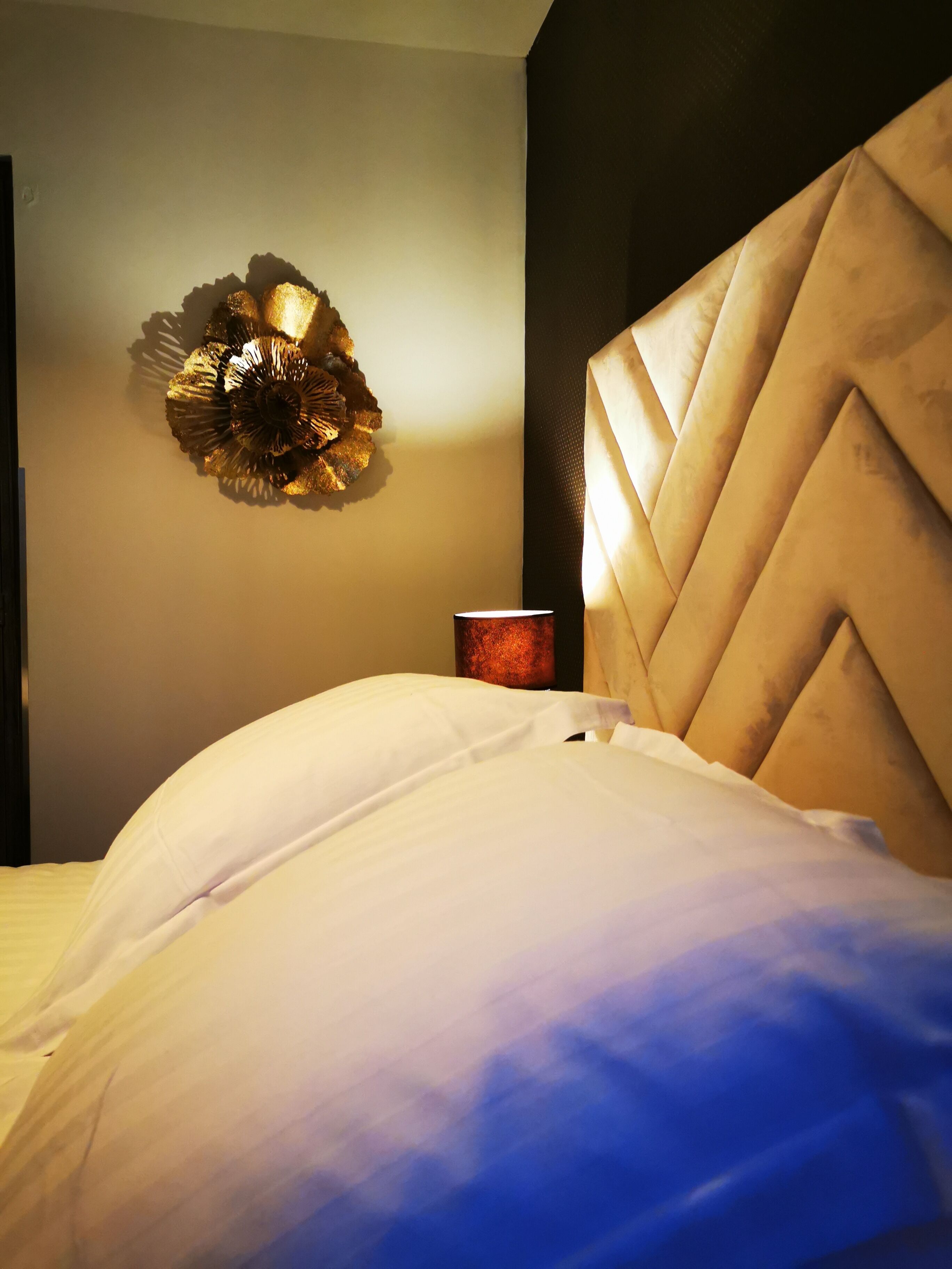 Cama com cabeceira branca e um detalhe decorativo na parede.