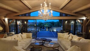 A spacious living area with a high ceiling and a chandelier, large windows, and a view of the outdoors. - La Villa Dune, Hôtel & Spa  (Gassin)