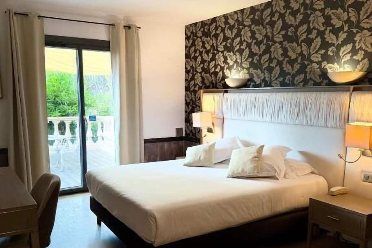 Une chambre d’hôtel avec un lit, une table de chevet, une lampe et une vue sur la verdure.