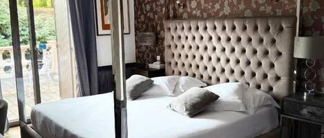 A four-poster bed with a tufted headboard, a bedside table, and a nightstand with a lamp.