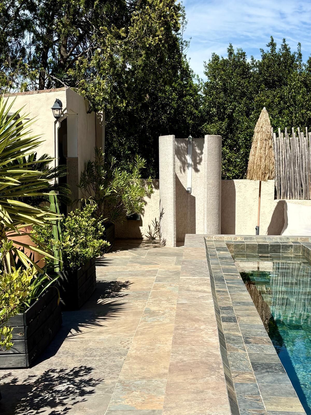 Un espace piscine doté d’un sol carrelé, d’une clôture en bois et de diverses plantes.