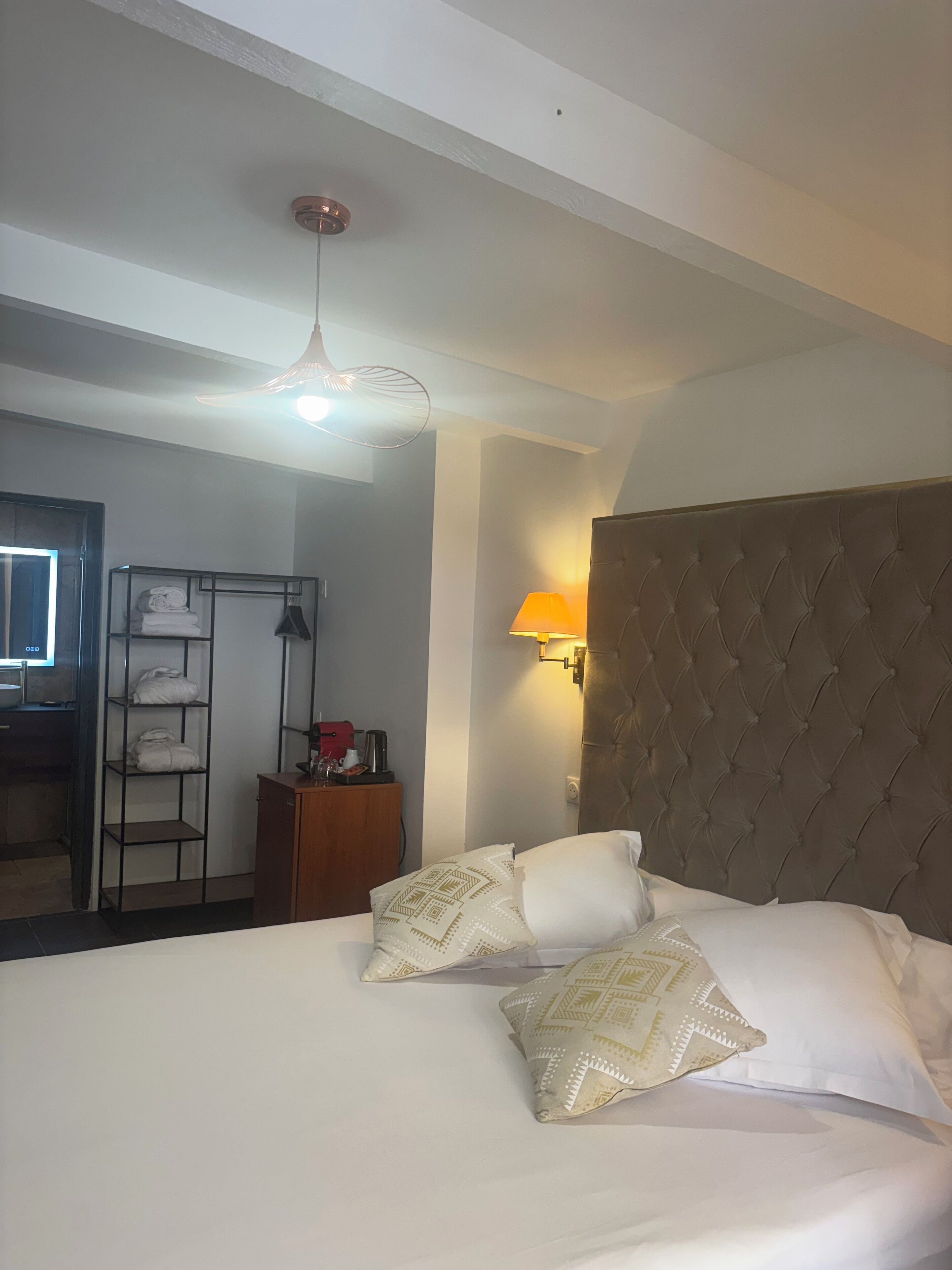 Une chambre d’hôtel avec un grand lit, une tête de lit en bois, une lampe de chevet, une armoire et une étagère avec des serviettes pliées.