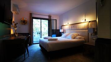 A hotel room with a bed, a desk, a chair, a nightstand, a lamp, and a view of the outdoors through a sliding door.