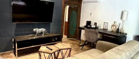 A modern living room with a large flat-screen TV mounted on a dark wall, a wooden entertainment unit, a beige sofa, and a small coffee table.