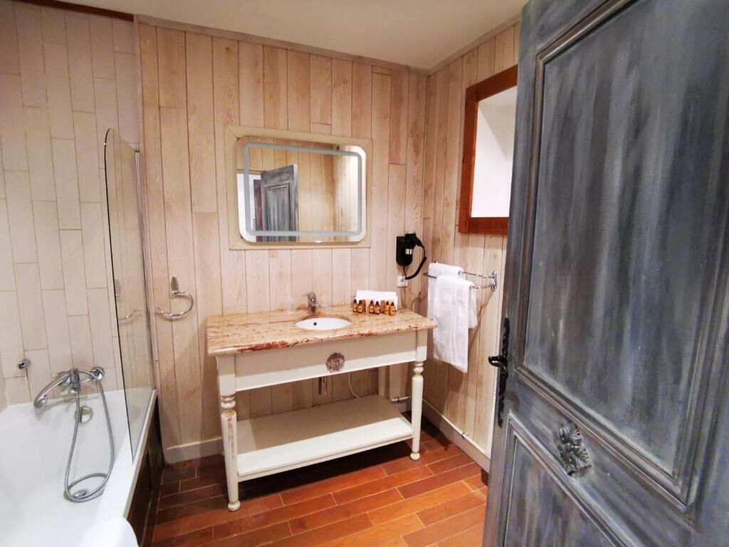 A bathroom with a wooden wall panel, a sink with a mirror above it, a towel hanging on a rack, and a door with a decorative handle.