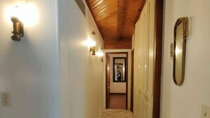 A narrow hallway with tiled flooring, wooden ceiling beams, and wall-mounted light fixtures. - Charming 7-bedroom house in Cauterets (Cauterets)