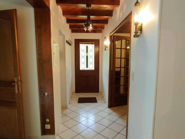 Un couloir avec une porte en bois, un sol carrelé et une fenêtre ornée de vitraux.