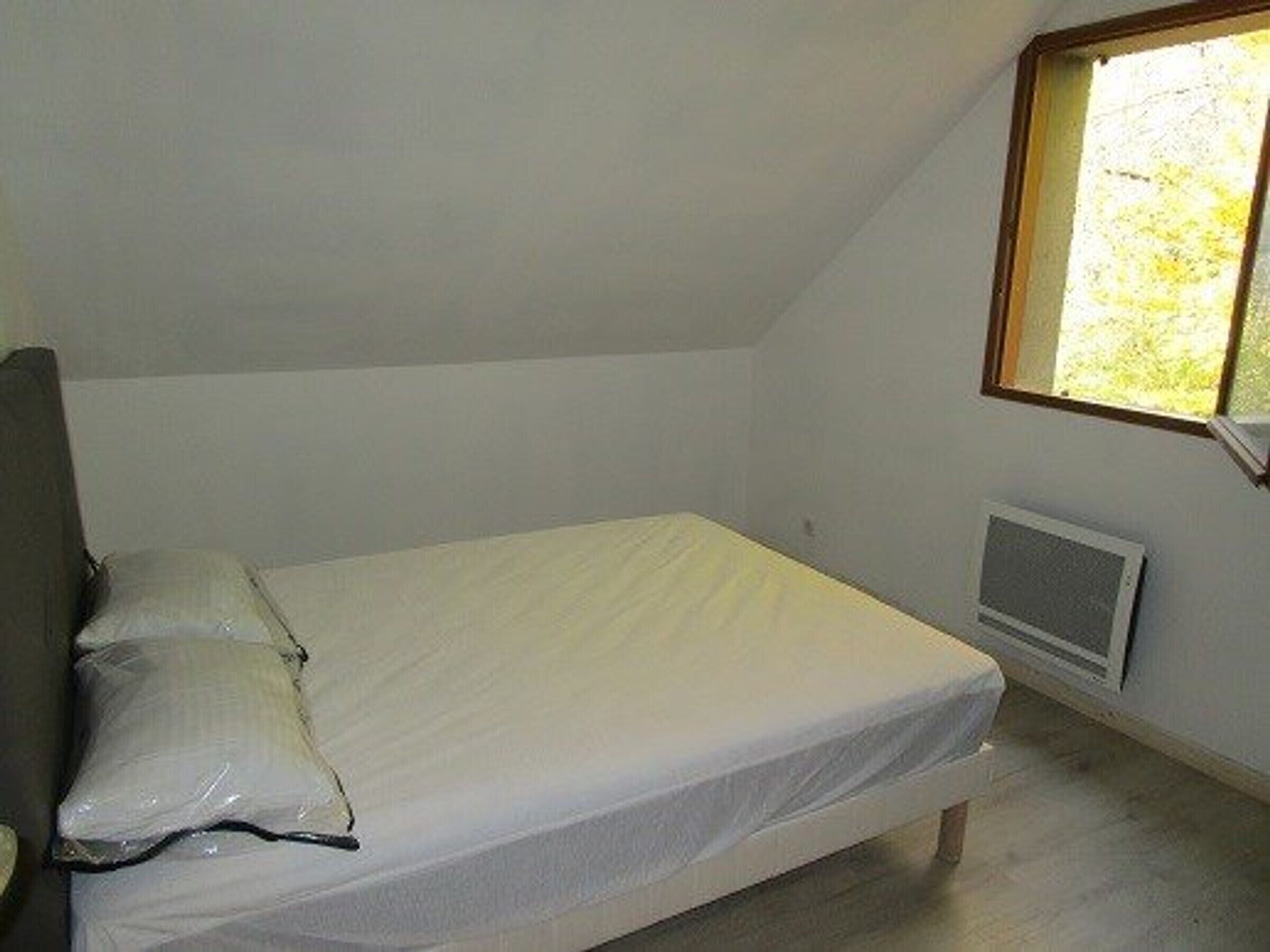 Una habitación pequeña con cama individual, techo inclinado y ventana que proporciona luz natural.