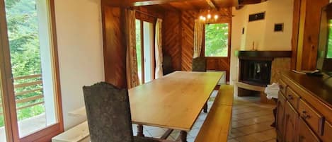 Un intérieur en bois avec une grande table à manger, des chaises, un lustre et une cheminée.