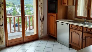 A kitchen with wooden cabinets, a dishwasher, and a view of a residential area through a sliding glass door. - Charming 7-bedroom house in Cauterets (Cauterets)