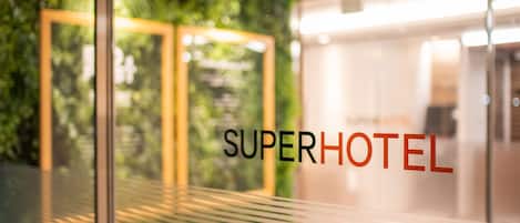 A glass door with the text "SUPERHOTEL" and a view of a green wall and a modern interior.