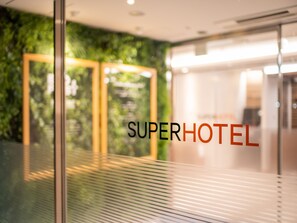 A glass door with the text "SUPERHOTEL" and a view of a green wall and a modern interior. - Super Hotel Gotemba - 1 (Gotemba)