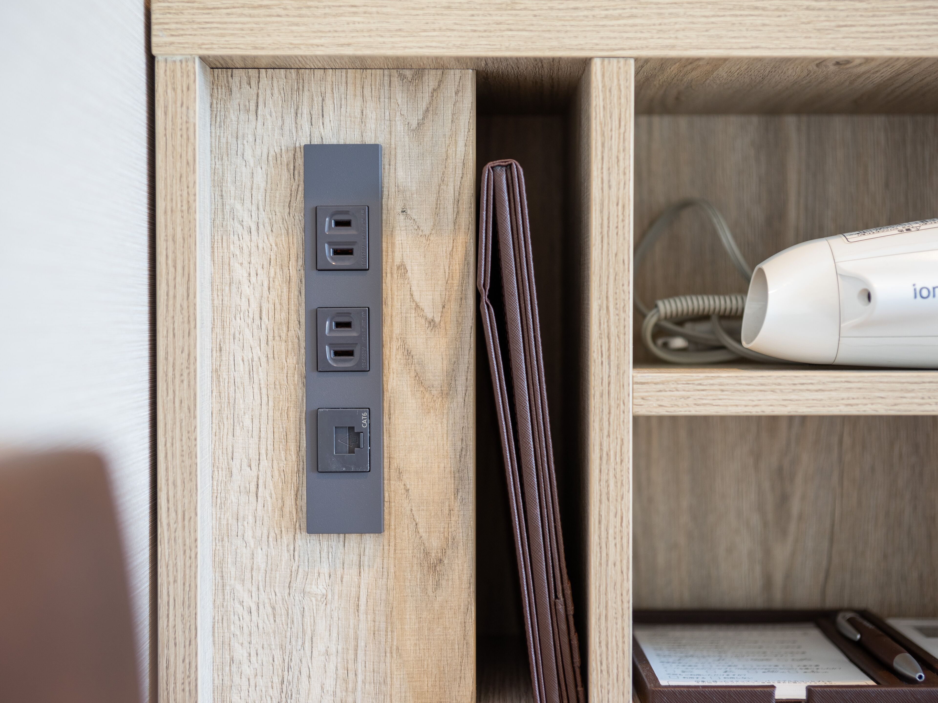 A wooden cabinet with a power strip, a wallet, and a white device on a shelf.