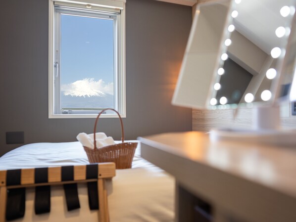 A bedroom with a bed, a window with a view of a mountain, a basket, a chair, and a vanity with lights. - Super Hotel Gotemba - 1 (Gotemba)