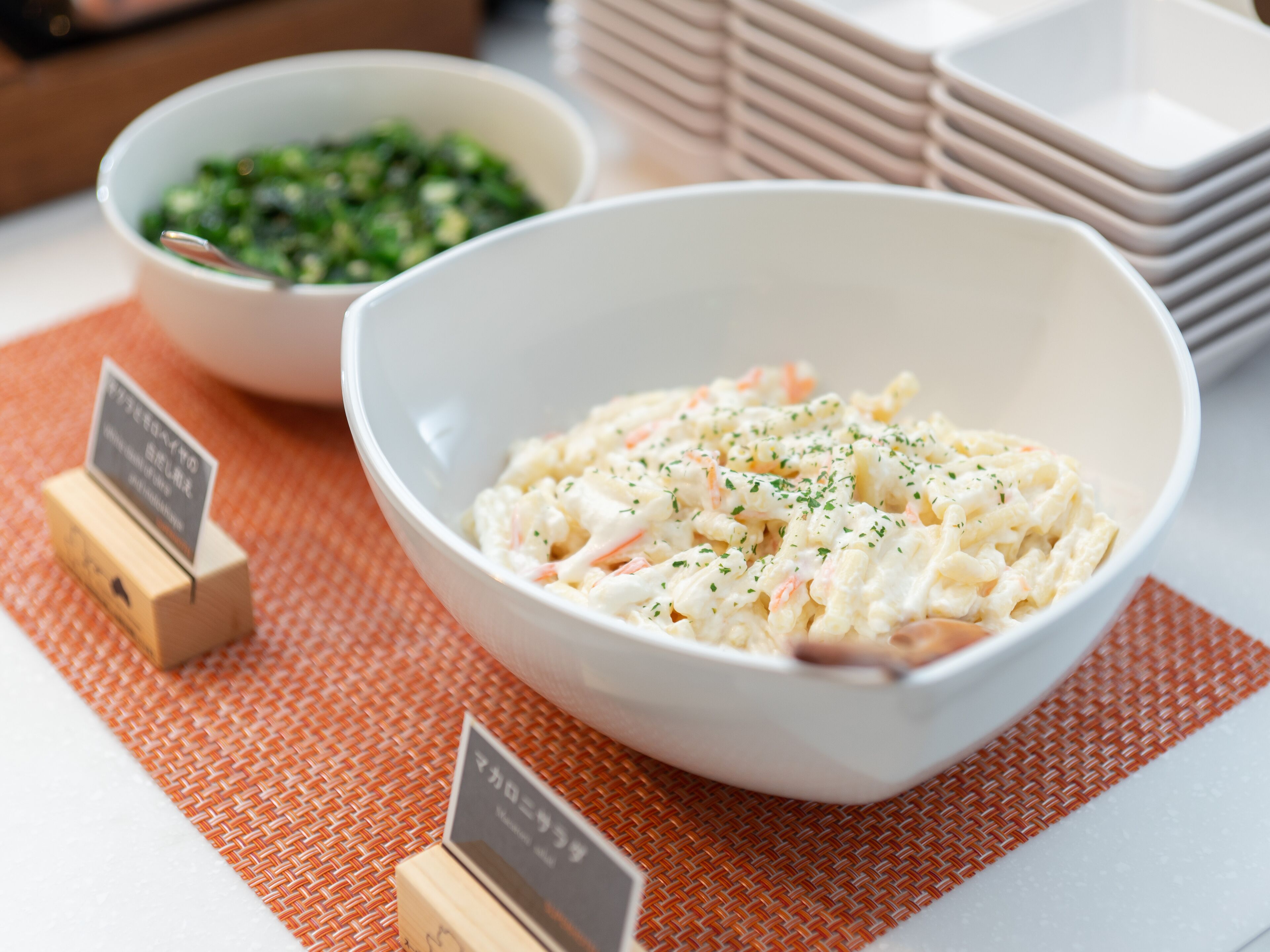 A table with two bowls of food, a woven placemat, and stacked plates.