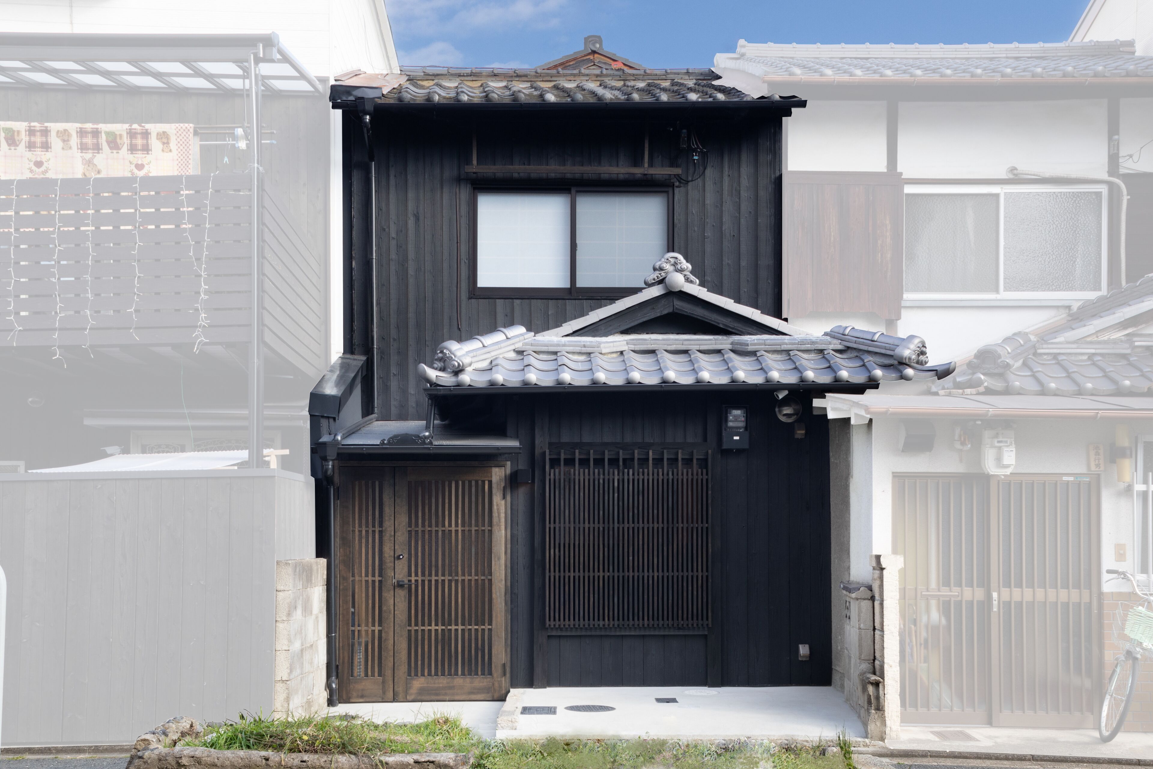 A traditional Japanese house with a dark wooden exterior, a tiled roof, and a sliding door.