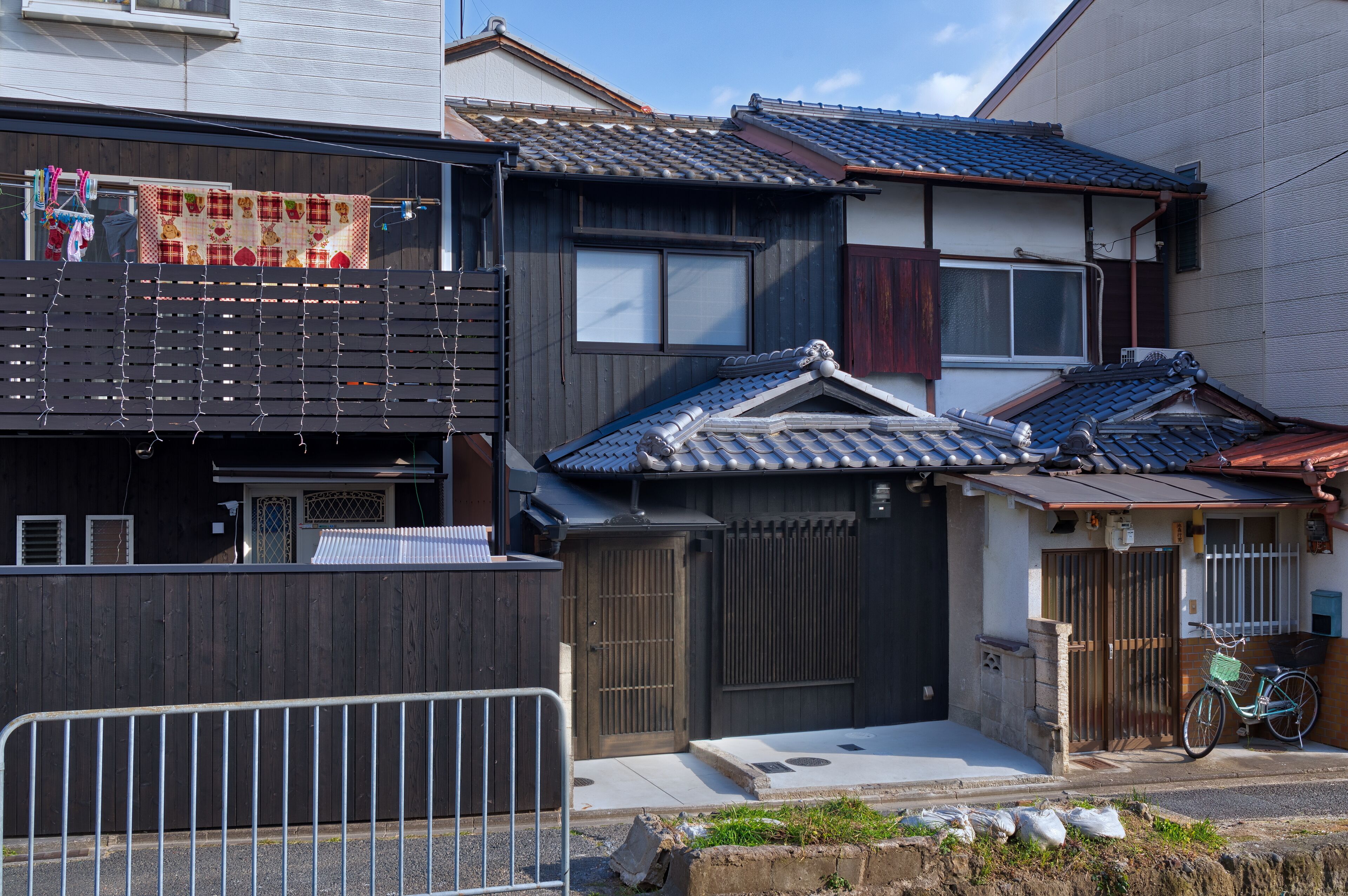 Une maison traditionnelle japonaise, avec un toit recouvert de tuiles, des murs en bois et un vélo garé à l’extérieur.