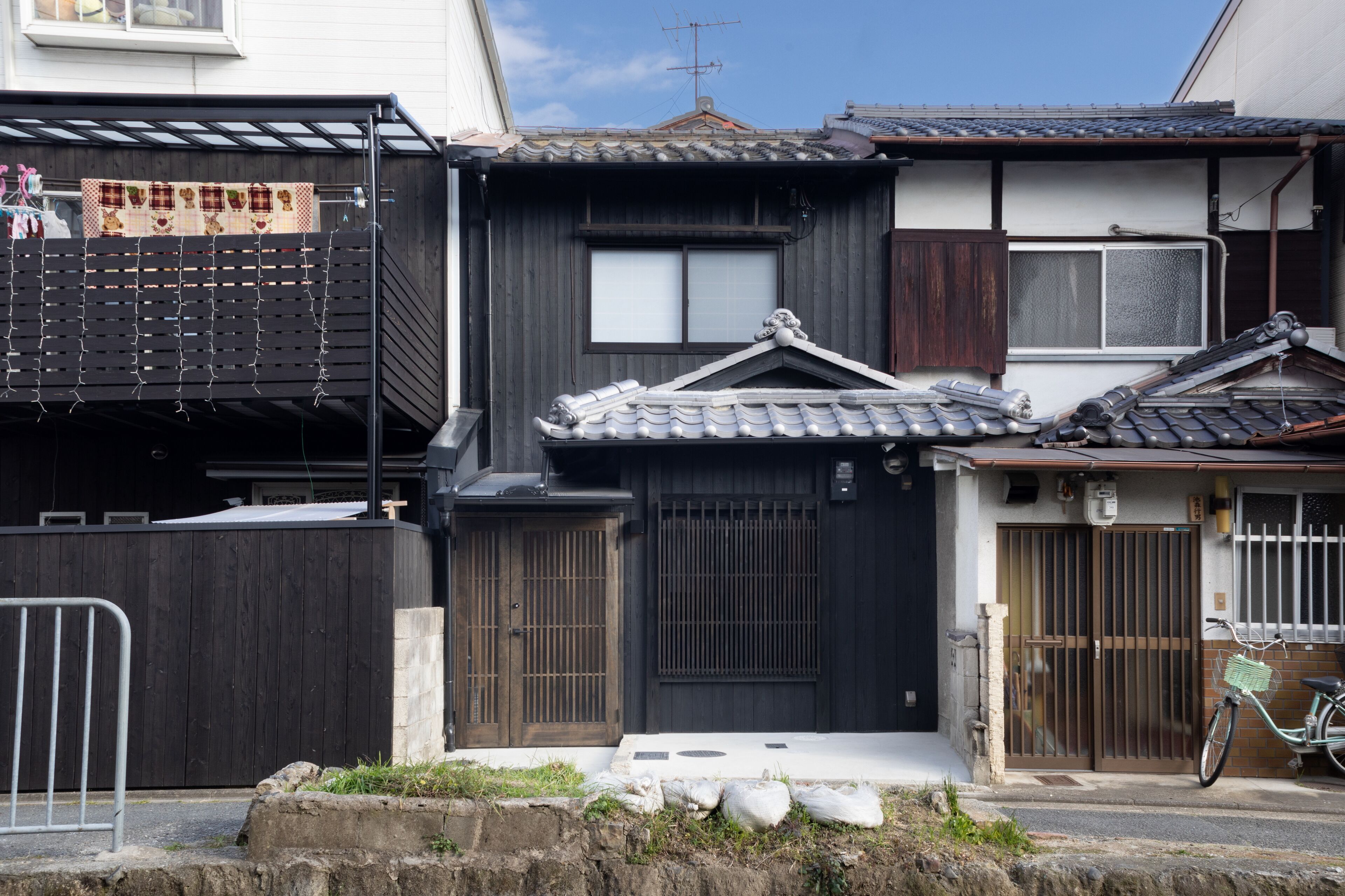 A traditional Japanese house with a dark wooden exterior, a tiled roof, and a bicycle parked outside.