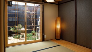 Una habitación japonesa tradicional con suelo de tatami, puertas correderas con vista al jardín, una lámpara de bambú y aire acondicionado montado en la pared.