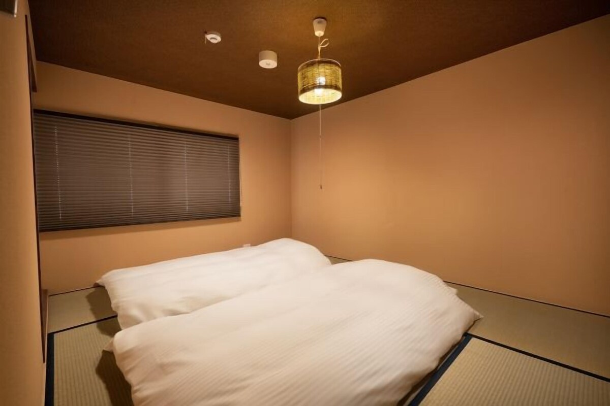 Een slaapkamer met een bed, een raam met zonwering en een hanglamp.