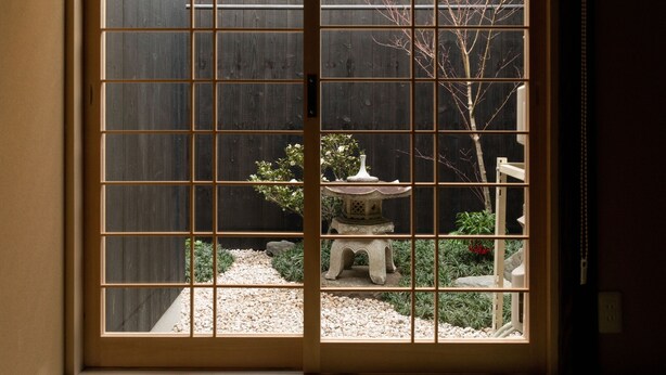 Una puerta corrediza japonesa tradicional con vistas a un jardín que incluye un farol de piedra y un árbol pequeño.
