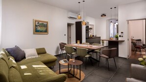 A modern living room with a green sofa, a dining table with chairs, and a kitchen area in the background. - Luxury Sea View Apartment Altana (Pula)