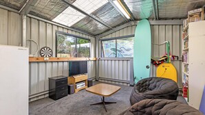 A compact room with a dartboard, a television, a surfboard, and a bookshelf. - Willan - 43 Powling Street (Port Fairy)