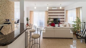 Ein modernes Wohnzimmer mit einer Couch, einer Essecke mit Barhocker, einer Küchenzeile und einem Fernseher.