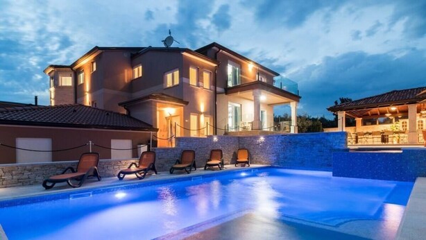 Ein modernes Haus mit Swimmingpool, Liegestühlen und gut beleuchteter Fassade.