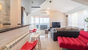 Ein modernes Wohnzimmer mit Steinwand, Flachbildfernseher, einem roten Sofa und einem Essbereich mit roten Stühlen.