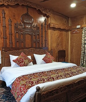 A wooden bed with intricate carvings, a patterned bedspread, and matching pillows. - Golden Crest Houseboats (Srinagar)