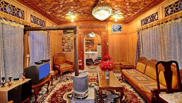 A traditional room with a patterned ceiling, a chandelier, a sofa set, a television, and a decorative table. - Golden Crest Houseboats (Srinagar)