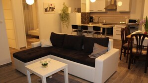 En moderne stue med en hjørnesofa, et lille hvidt bord og et køkken i baggrunden.