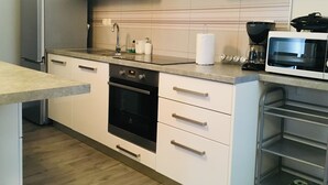 Et moderne køkken med hvide skabe, et rustfrit stål køleskab, en indbygget ovn og en mikroovn.
