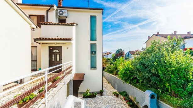 A narrow alleyway with a white building featuring a door and a window, flanked by greenery and a stone-tiled path. - Comfortable apartment PUH (Pula)