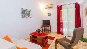 A hotel room with a bed, a chair, a TV, a small table with a plant, and a window with red curtains. - Comfortable apartment PUH (Pula)