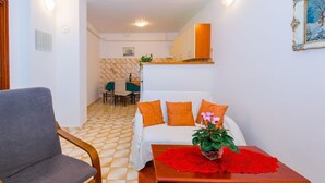 A room with a checkered floor, a grey armchair, a white sofa with orange cushions, and a wooden table with a red table runner and a potted plant. - Comfortable apartment PUH (Pula)
