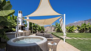 Un bain à remous installé sous une pergola, du mobilier d’extérieur et une vue sur les montagnes.