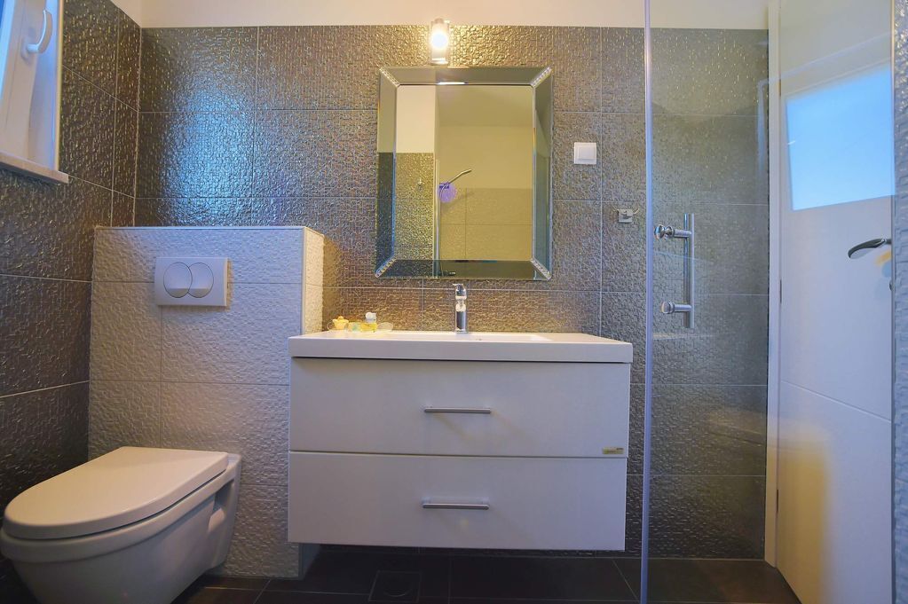 A bathroom with a toilet, a sink with a mirror, and a shower area.