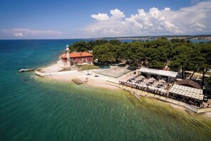 Une zone côtière comprenant un phare, une plage et un espace extérieur abrité avec des parasols, aménagé pour accueillir des clients.