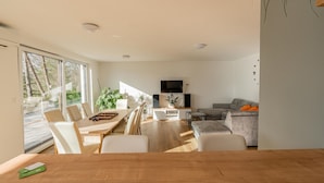 A modern living room with a dining area, a grey sofa, and a television on the wall. - Nature View House With Sauna (Tolmin)