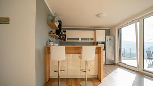 A modern kitchen with two white bar stools, wooden cabinets, and a built-in refrigerator. - Nature View House With Sauna (Tolmin)