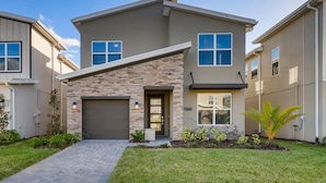 A two-story residential building with a stone facade, a garage, and a well-maintained lawn. - 5Bd Home, Storey Lake with Private Pool 14 Guests - Private Pool - 2773 BD (Kissimmee)