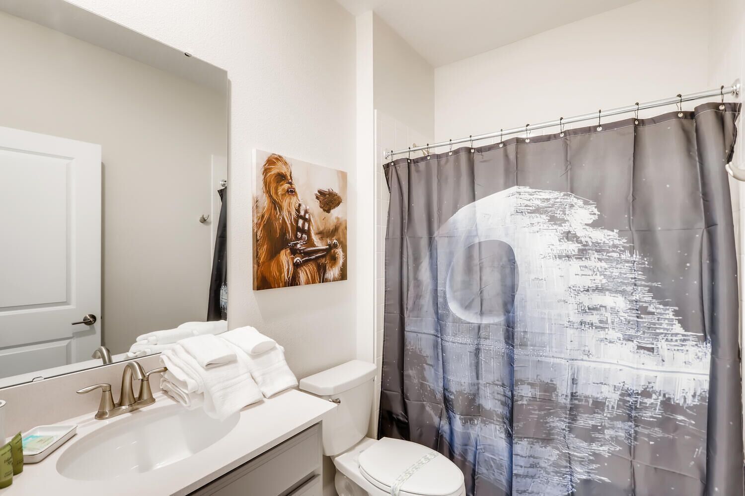 Un baño con lavamanos blanco, inodoro y cortina de ducha con diseño de paisaje urbano.
