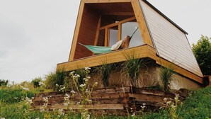 A modern, wooden cabin with a slanted roof, a hammock on the deck, and a natural surrounding. - Panorama Glamping Visole (Slovenska Bistrica)