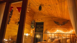 A cozy wooden cabin bedroom with a bed, a decorative wall sign, and a small table with a lamp. - Panorama Glamping Visole (Slovenska Bistrica)