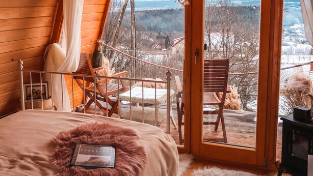 A cozy wooden cabin bedroom with a large bed, a view through a glass door to a snowy landscape, and a rustic interior. - Panorama Glamping Visole (Slovenska Bistrica)