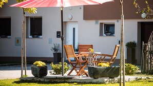 Een terras met een rode parasol, houten stoelen en potplanten.