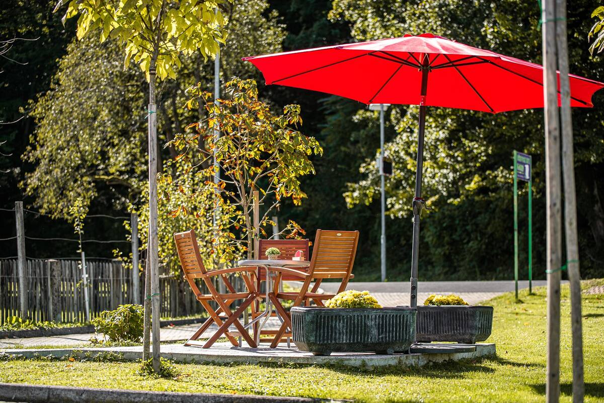 Een terras met een rode parasol, houten stoelen en een plantenbak.