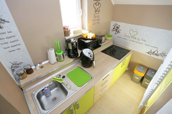 A compact kitchen with a sink, stove, and microwave. There are jars of spices and a coffee maker on the counter.